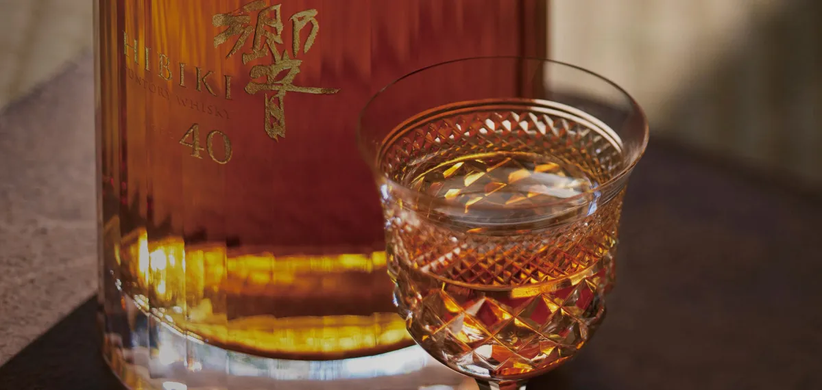 A bottle of Hibiki 40 Years whiskey beside a filled glass on a table.