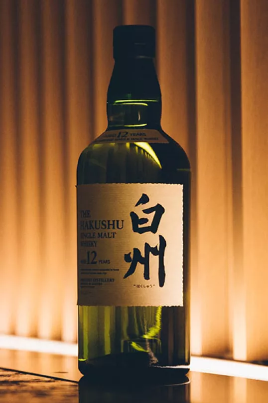 Green bottle of Suntory Hakushu Whisky against light curtain