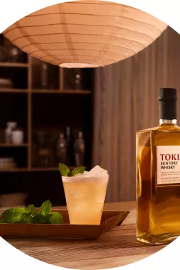 Suntory Whisky Toki sitting on modern wooden bar next to whisky sour cocktail