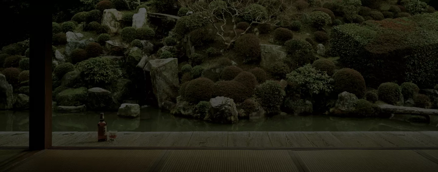 Whisky bottle and glass with ice overlooking Japanese rock garden