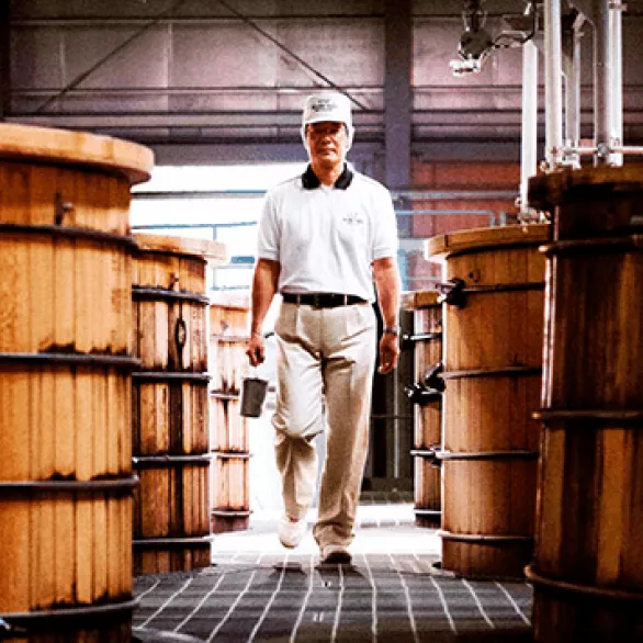 Man in Suntory Whisky uniform walking down row of oak barrels at Hakushu Distillery