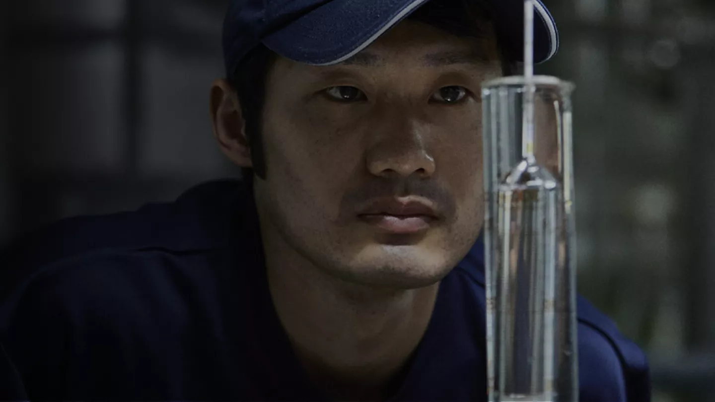 Japanese man staring at distilling syringe inside a percolator facing the viewer