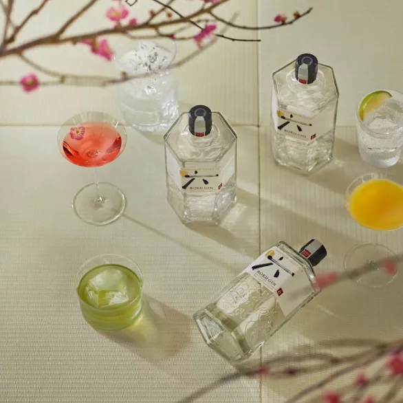 Three bottles of Roku Gin on Tatami mats with filled glasses and pink cherry blossom twigs.