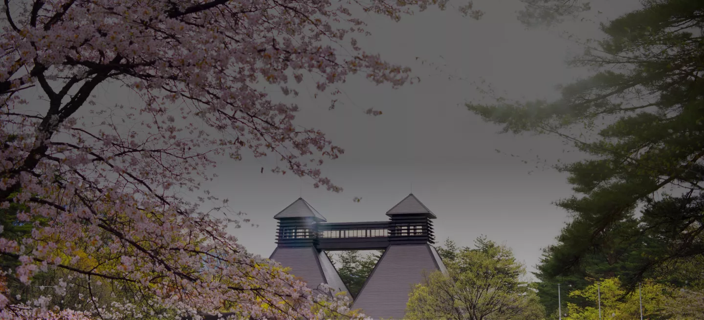 Pink flowering tree sits in front of the twin rooftops of the Hakushu Distillery