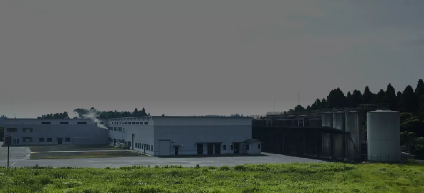 Large Suntory Osumi distillery building nestled between green grass and blue skies