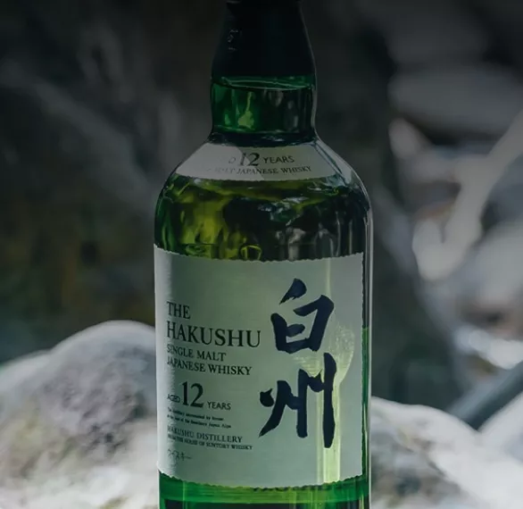 Close up of green Suntory Whisky Hakushu bottle sitting on gray rocks outside