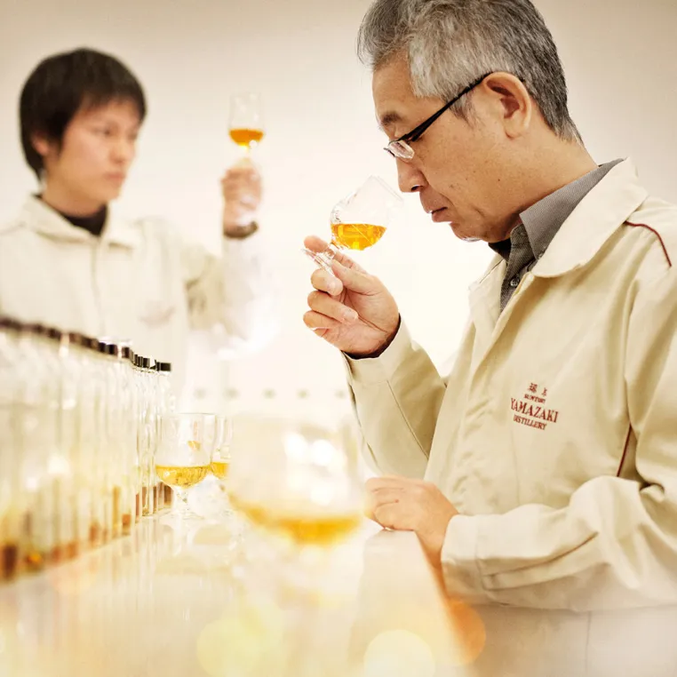 People in lab coats inspecting whiskey glasses at a distillery.