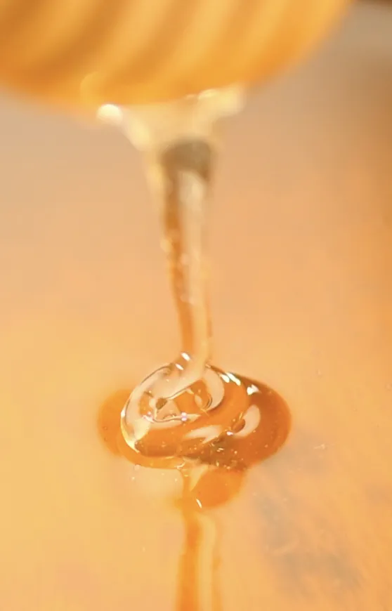 Honey dripping from spoon onto a surface, reflecting golden light.