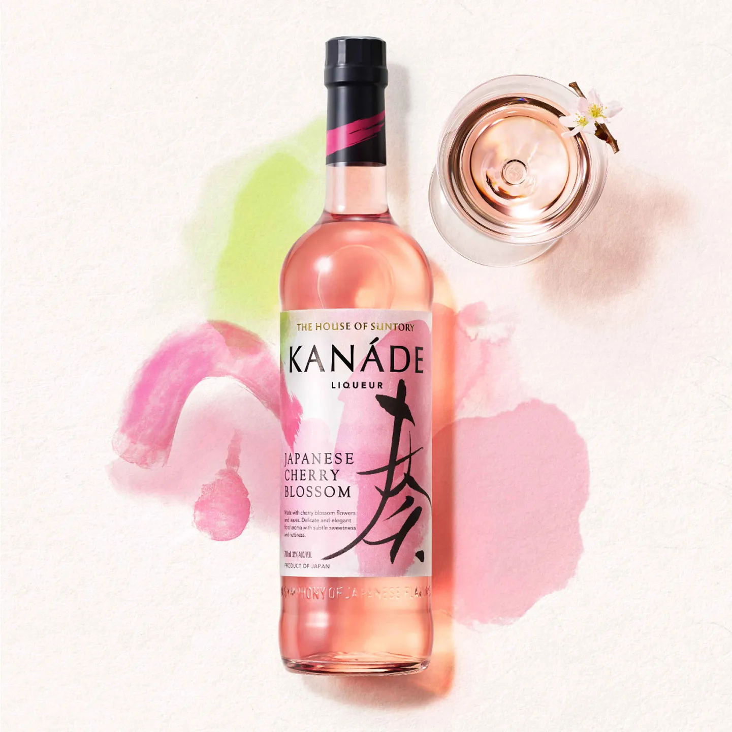 A bottle of Kanade Japanese Cherry Blossom liqueur next to a glass filled with its pink liquid, surrounded by pastel watercolor splashes.