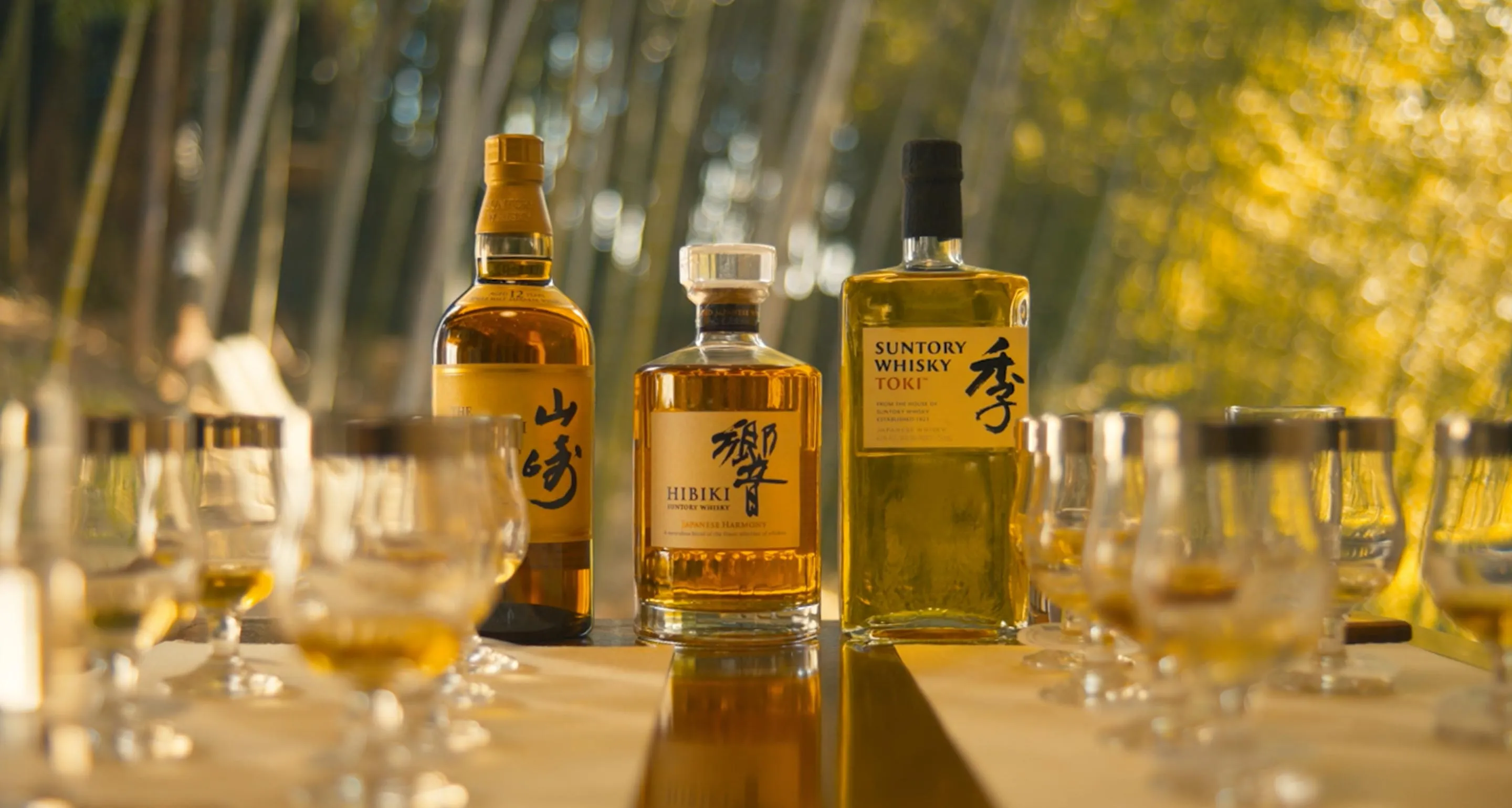 Yamazaki, hibiki and toki bottles display on table surrounded by whisky glasses