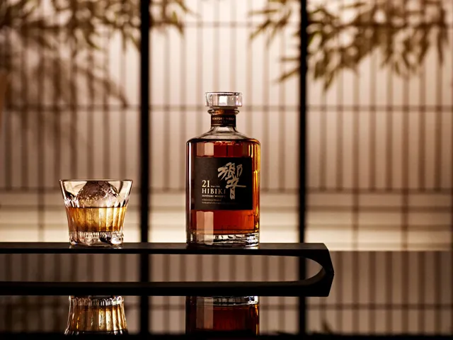 Bottle of Hibiki 21 Japanese whisky with a glass of whisky on the rocks, served with a large ice sphere, in an elegant Japanese setting.