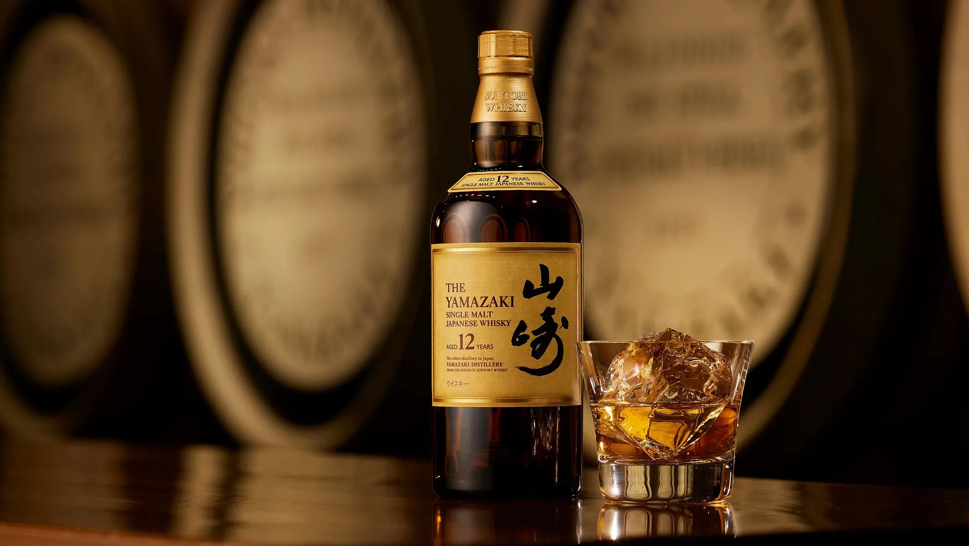 A bottle of Yamazaki 12-Year-Old Single Malt Japanese Whisky next to a glass with ice and golden whisky, set against a blurred background.